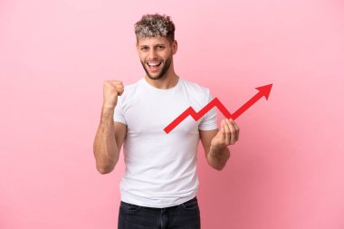 Pembe arka planda izole edilmiş yakışıklı beyaz bir adam yükselen bir oku tutuyor ve zaferi kutluyor.