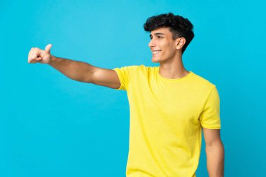 Arjantinli genç adam arka planda izole edilmiş bir şekilde baş parmak hareketi yapıyor.