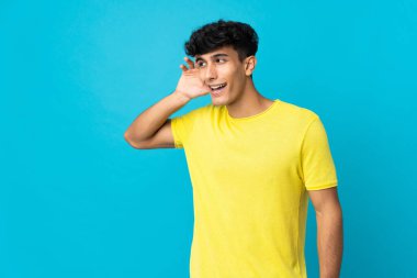 Arjantinli genç adam arka planda izole edilmiş bir şekilde bir şeyler dinlerken elini kulağına koydu.