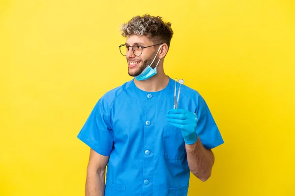 Dentysta Biały Mężczyzna Trzyma Narzędzia Izolowane Żółtym Tle Patrząc Bok — Zdjęcie stockowe