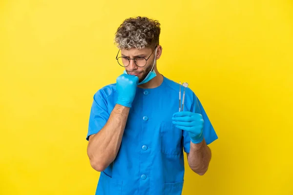 Dentysta Kaukaski Mężczyzna Trzyma Narzędzia Izolowane Żółtym Tle Mając Wątpliwości — Zdjęcie stockowe