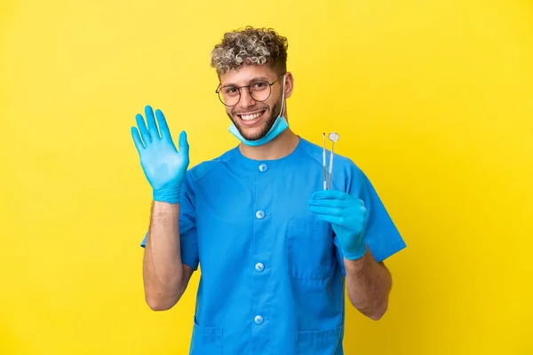 Dentysta Kaukaski Mężczyzna Trzyma Narzędzia Izolowane Żółtym Tle Salutując Ręki — Zdjęcie stockowe