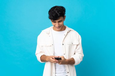 Arjantinli genç adam arka planda izole edilmiş cep telefonuyla mesaj gönderiyor.