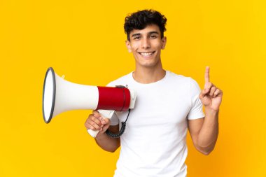 Arjantinli genç adam sarı arka planda izole edilmiş elinde bir megafonla harika bir fikre işaret ediyor.