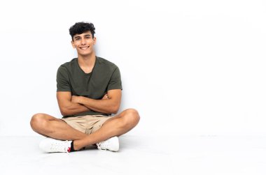 Arjantinli genç adam yerde oturuyor ve kollarını ön cephede kavuşturuyor.