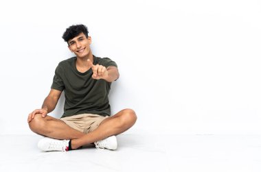 Genç Arjantinli adam yerde oturuyor ve parmağını kaldırıyor.