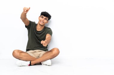 Yerde oturan genç Arjantinli adam gülümserken seni işaret ediyor.