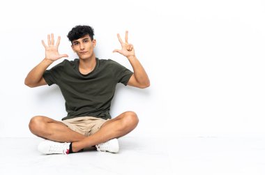 Genç Arjantinli adam yerde oturmuş parmaklarıyla sekizi sayıyor.