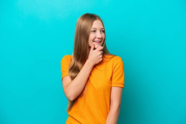 Genç Rus kadın mavi arka planda izole edilmiş, yan tarafa bakıyor ve gülümsüyor.