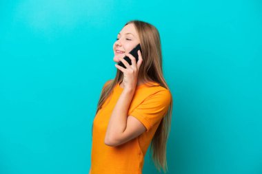 Mavi arka planda izole edilmiş genç bir Rus kadın cep telefonuyla biriyle sohbet ediyor.