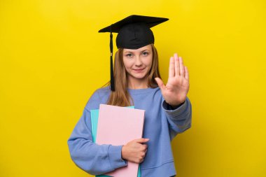 Genç Rus öğrenci, sarı arka planda izole edilmiş. Durma hareketi yapıyor.