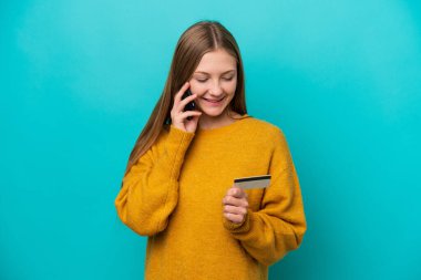 Genç Rus kadın mavi arka planda izole edilmiş cep telefonuyla kredi kartıyla alışveriş yapıyor.