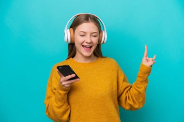 Genç Rus kadın mavi arka planda izole edilmiş, hareketli bir rock hareketi yaparak müzik dinliyor.