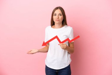 Genç Litvanyalı bir kadın pembe arka planda izole edilmiş, aşağıya doğru ok atıyor ve üzgün bir ifadeyle