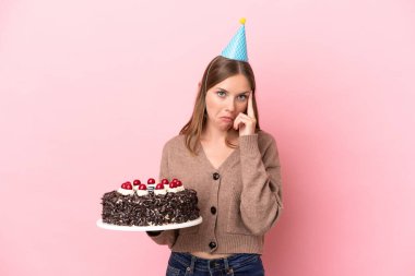 Elinde doğum günü pastası tutan Litvanyalı genç bir kadın pembe arka planda izole edilmiş bir fikir düşünüyor.