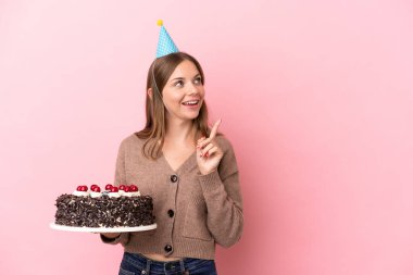 Elinde doğum günü pastası tutan Litvanyalı genç bir kadın pembe arka planda izole edilmiş bir şekilde çözümü bulmak için parmağını kaldırıyor.