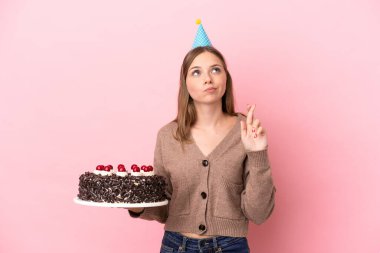 Elinde doğum günü pastası tutan genç Litvanyalı kadın pembe arka planda izole edilmiş ve şans diliyor.