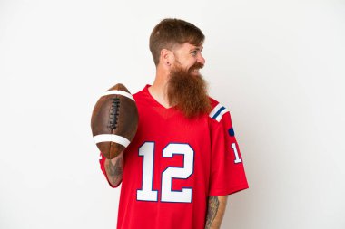 Beyaz arka planda ragbi oynayan beyaz tenli genç, beyaz bir adam yan tarafa bakıyor ve gülümsüyor.