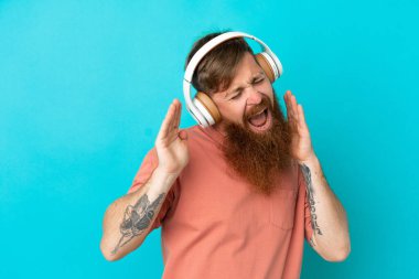 Kırmızımsı beyaz adam mavi arka planda izole edilmiş müzik ve dans dinliyor.