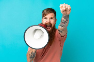 Mavi arka planda izole edilmiş genç beyaz adam megafondan bir şey duyurmak için bağırıyor.