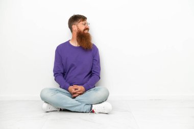 Beyaz arka planda izole bir şekilde yerde oturan Kafkasyalı genç adam.