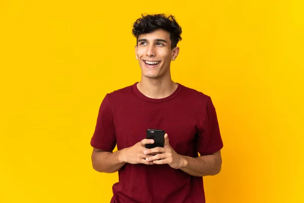 Joven Argentino Aislado Sobre Fondo Amarillo Usando Teléfono Móvil Mirando — Foto de Stock