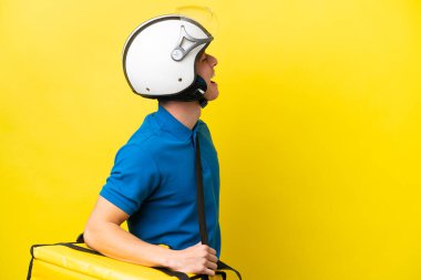 Sırt çantalı genç Brezilyalı adam sarı arka planda izole edilmiş. Yan pozisyonda gülüyor.