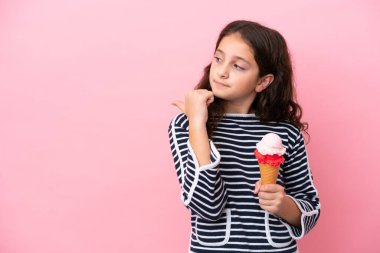 Küçük beyaz kız pembe arka planda izole edilmiş bir dondurma tutuyor. Yan tarafı göstererek bir ürün sunuyor.