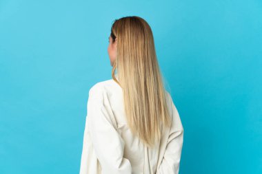 Genç sarışın kadın mavi arka planda izole edilmiş ve arkasına bakıyor.