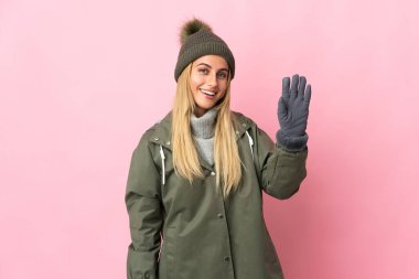 Kış şapkalı genç kadın pembe arka planda izole edilmiş mutlu bir ifadeyle selamlıyor.