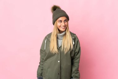 Pembe arka planda izole edilmiş, kış şapkalı genç bir kadın yukarı bakarken bir fikir düşünüyor.