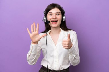 Mor arka planda izole edilmiş kulaklıkla çalışan pazarlamacı Rus kadın parmaklarıyla altı kişi sayıyor.