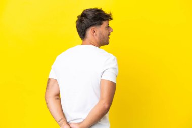 Beyaz tenli yakışıklı adam sarı arka planda izole edilmiş ve arkasına bakıyor.