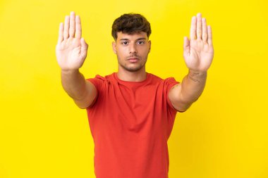 Sarı arka planda izole edilmiş beyaz, yakışıklı genç adam dur hareketi yapıyor ve hayal kırıklığına uğruyor.