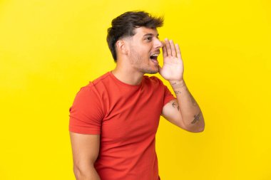 Sarı arka planda izole edilmiş, ağzı sonuna kadar açık bağıran beyaz, yakışıklı genç bir adam.