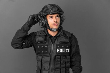 SWAT 'ın beyaz adamı gri arka planda izole edilmiş. Şüpheleri var ve kafası karışmış bir yüz ifadesi var.