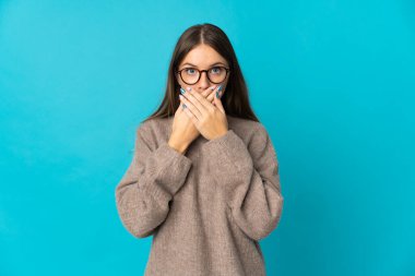 Genç Litvanyalı kadın mavi arka planda izole edilmiş, ağzı elleriyle kapatıyor.