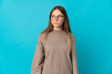 Genç Litvanyalı kadın mavi arka planda izole edilmiş. Şüpheli hareketler yapıyor.