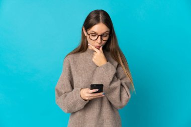Genç Litvanyalı kadın mavi arka planda izole edilmiş düşünüyor ve bir mesaj gönderiyor.