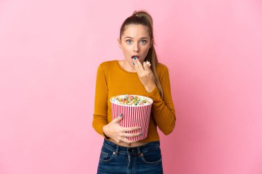 Genç Litvanyalı bir kadın pembe arka planda izole edilmiş. Elinde koca bir kova patlamış mısır var.