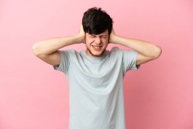Pembe arka planda izole edilmiş genç Rus adam hayal kırıklığına uğramış ve kulaklarını kapatmış.