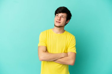 Genç Rus adam mavi arka planda izole edilmiş gülümserken yukarı bakıyor.