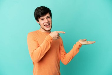 Genç Rus bir adam mavi arka planda izole edilmiş. Kopyalama alanı hayali bir ilan vermek için avucunun içinde duruyor.