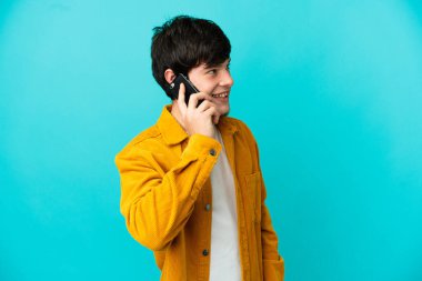 Genç Rus adam mavi arka planda izole edildi. Cep telefonuyla birileriyle sohbet ediyor.