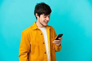 Genç Rus adam mavi arkaplanda izole edilmiş cep telefonuyla mesaj ya da e-posta gönderiyor.