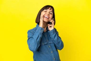 Sarı arka planda izole edilmiş cep telefonu kullanan hamile bir kadın ağzı açık bağırıyor.