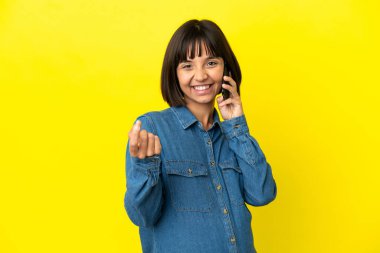 Sarı arka planda izole edilmiş cep telefonu kullanan hamile bir kadın para hareketi yapıyor.