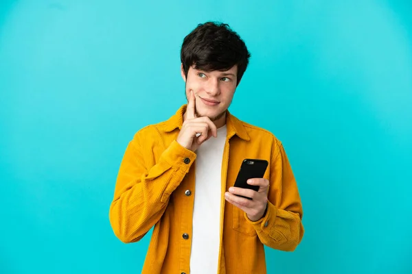 Young Russian Man Isolated Blue Background Using Mobile Phone Thinking — 图库照片