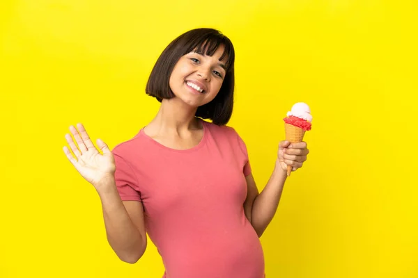 Беременная Женщина Держит Корнет Мороженое Изолированы Желтом Фоне Салютуя Руки — стоковое фото