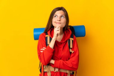 Sarı arka planda izole edilmiş büyük sırt çantalı Slovak dağcı kadın şüpheleri ve düşünceleri var.